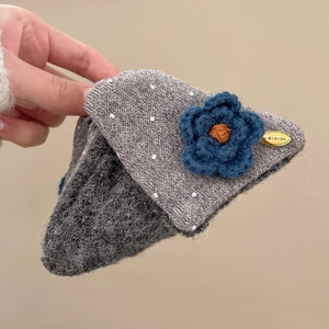 Détail de la pince à cheveux grise tricotée à pois avec fleur bleue et logo doré