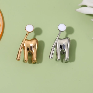 Detail of silver and gold metal toothbrush and tooth enamel pins on green background