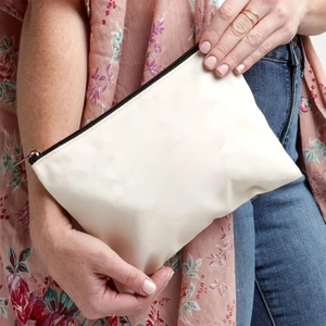 Close-up of a hand holding an off-white canvas storage pouch with a black zipper detail