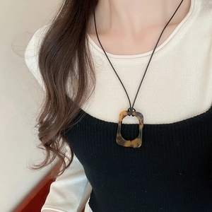 Close-up of tortoise shell resin rectangular pendant with black cord on a model
