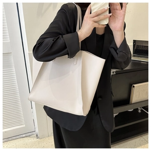 Detail of off-white PU leather tote bag held by a model in a minimalist office setting