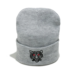 Close-up of a grey knitted beanie featuring a detailed tiger head embroidery on the cuff