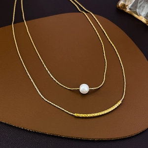 Detail of double-layer gold necklace featuring a white pearl and textured metal tube