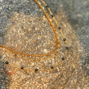 Close-up of triple-layered gold stainless steel necklaces with sleek black beads on rock