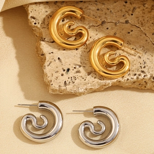 Detail of twisted spiral hoop earrings in gold and silver finish on textured stone