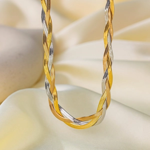 Macro detail of triple-layered gold and silver woven flat snake chain on silk fabric