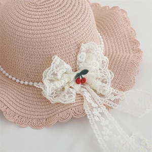 Detail of girls straw sun hat with pink lace bow, cherry embroidery and pearl trim