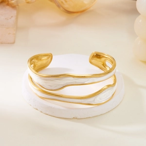 Detail of a gold wavy enamel bangle with elegant white double-layer fluid wave design