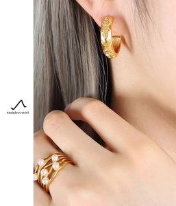 Macro detail of French vintage golden stainless steel earrings and pearl wave ring