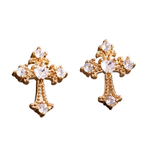 Dettaglio di orecchini a croce gotici dorati con zircone centrale a forma di cuore