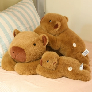 Three plush capybara soft toys in different sizes resting on a striped pillow