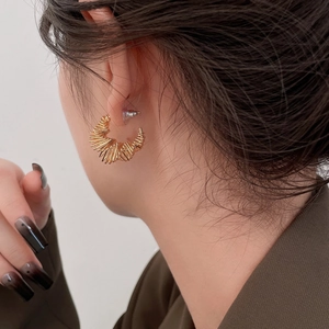 Detail of gold-plated spiral twist earrings worn by a model showing modern metallic texture