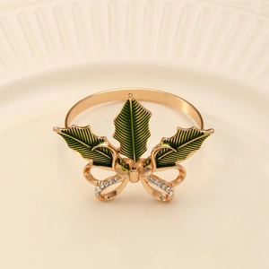 Détail d'un rond de serviette doré avec feuilles en émail vert et nœud en cristaux