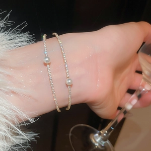 Close-up of double-layer gold bracelets with shimmering cubic zirconia and a central pearl