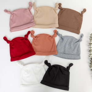 Vue à plat de bonnets tricotés pour bébé en plusieurs coloris comme rose et beige