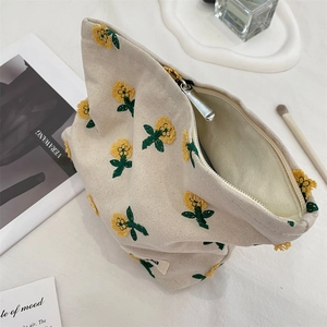 Détail de broderie florale sur trousse de maquillage en toile beige avec fermeture éclair