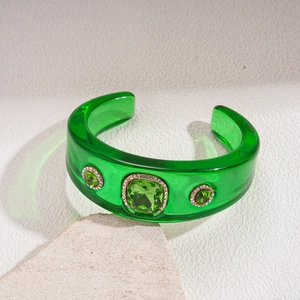 Detailed view of translucent green resin cuff bracelet with gold-rimmed emerald crystals