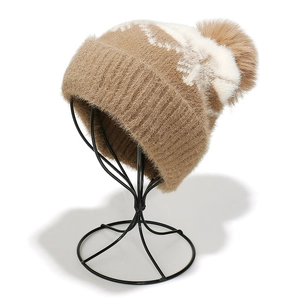 Detail view of winter knitted hat with white snowflake pattern and large faux fur pom-pom
