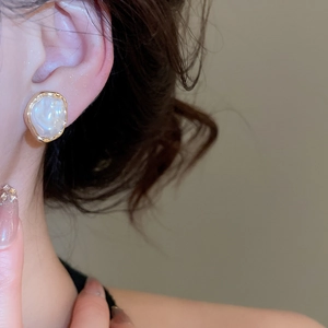 Detail of irregular baroque pearl earring with gold metallic edge on model's ear