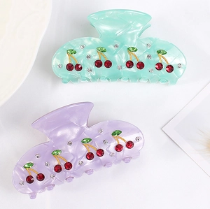 Detail of light green and purple acrylic hair claws with cherry rhinestone embellishments