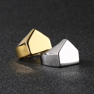 Close-up of polished gold and silver geometric pyramid rings on a textured black background