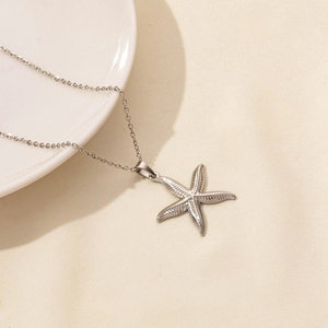 Close-up of a silver starfish pendant with textured engraving on a delicate chain