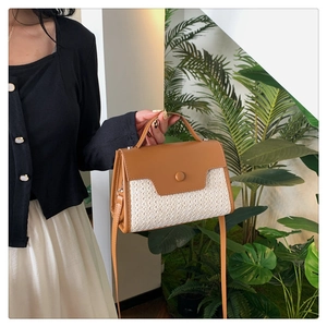 Détail d'un sac à main en paille et cuir marron tenu à la main avec rabat et bandoulière