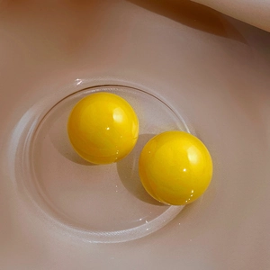 Macro view of bright yellow spherical acrylic stud earrings on a transparent glass tray