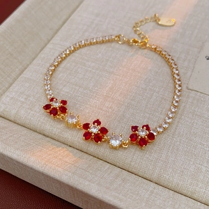 Detailed close-up of golden floral bracelet with red zircon flowers on beige fabric