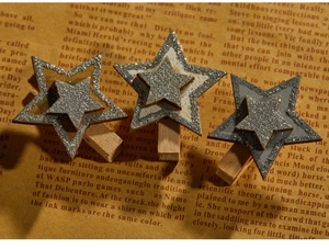 Close-up of three star-shaped wooden clips with sparkling gold, silver, and grey glitter finish