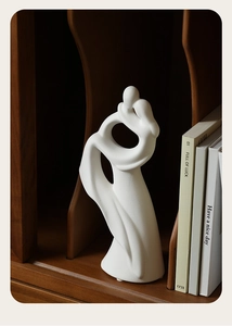 Close-up of white ceramic abstract couple sculpture on a dark wooden shelf