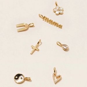 Close-up of gold pendants including MAMA letters, cross, and heart with shell inlay