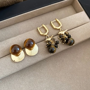 Detail of 18k gold bird earrings with tiger eye stone tassel in a beige velvet jewelry box