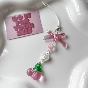 Pink cherry beaded phone charm with acrylic bow and heart hanging on a white wave plate