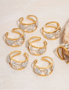 Detail of gold open rings with crystal heart and letter charms on a stone surface
