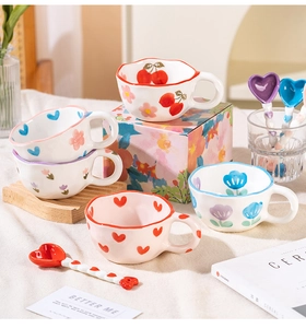 Detail of hand-painted wave-edge ceramic mugs with heart spoons in floral cherry patterns