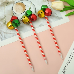 Three Christmas bell ballpoint pens with red and white striped barrels on a warm pink desk