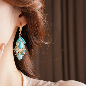 Détail de boucles d'oreilles bohèmes dorées avec turquoise et perles frangées sur modèle