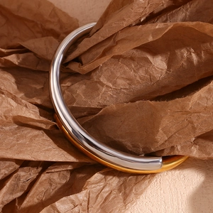 Artistic detail of a high-polish two-tone silver and gold layered open bangle on paper