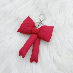 Vibrant red velvet bow keychain with silver metal clasp on a white faux fur background