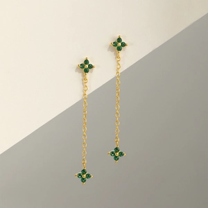 Detail of gold clover drop earrings featuring green stones and long delicate chains