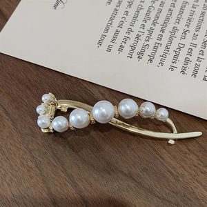 Elegant gold metal hair clip with white pearls on a dark wood and paper background