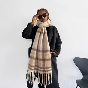 Close-up of a beige checkered mohair scarf with tassels paired with a stylish black coat