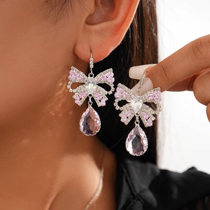 Detailed view of silver bow earrings featuring pink zircon teardrop pendants on model