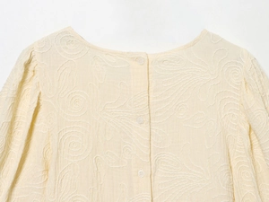 Détail de trois boutons blancs et broderie texturée sur le col de chemise crème