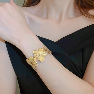 Close-up of golden flower open cuff bracelet with brushed metal texture on a female wrist
