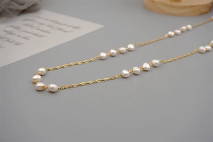 Close-up of golden chain necklace with baroque pearls on elegant silk display