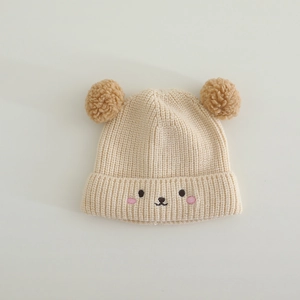 Detail of baby beige knit hat with plush brown pom-poms and cute bear embroidery