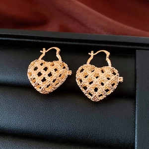 Detailed macro shot of gold hollow basket weave heart earrings on a black leather stand