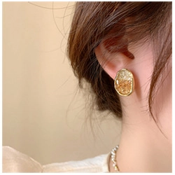 Detail of 18k gold plated earring with amber resin inlay worn on a female ear